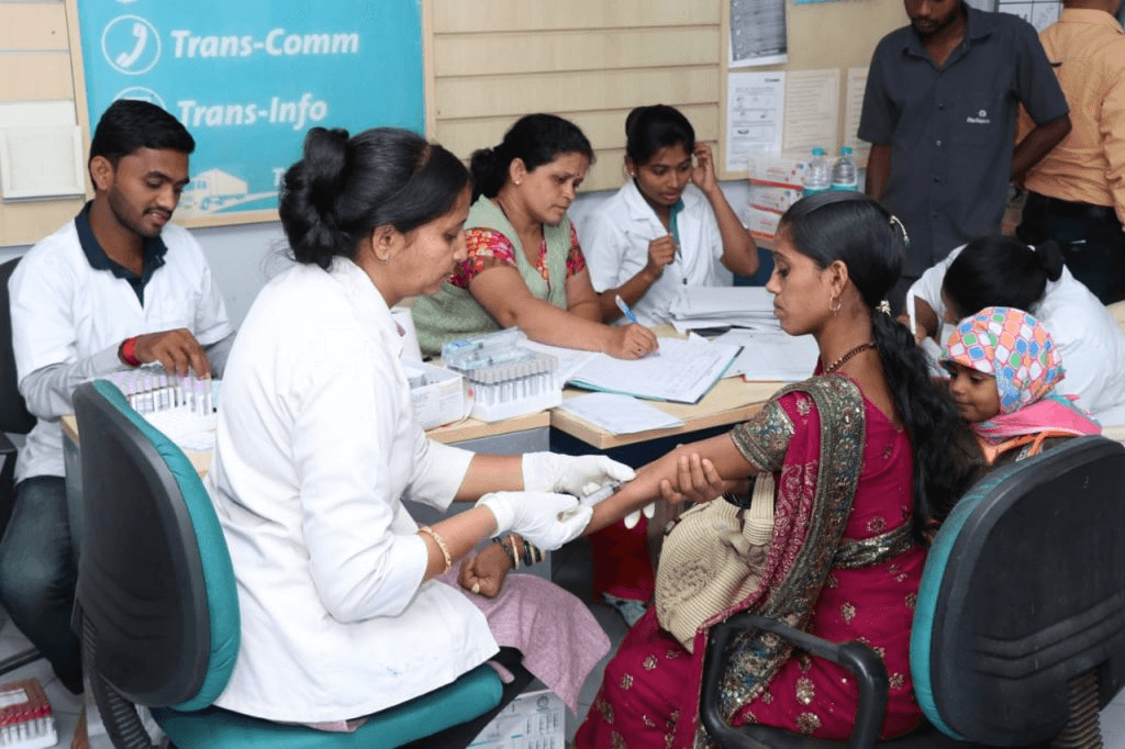 Health workers collecting blood samples from residents at an indoor screening camp